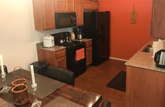 kitchen featuring black appliances, dark hardwood / wood-style flooring, light stone counters, and sink