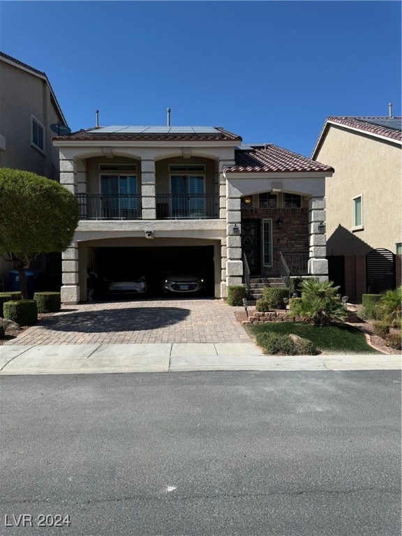 view of front facade featuring decorative driveway, roof mounted solar panels, a balcony, stone siding, and a tiled roof