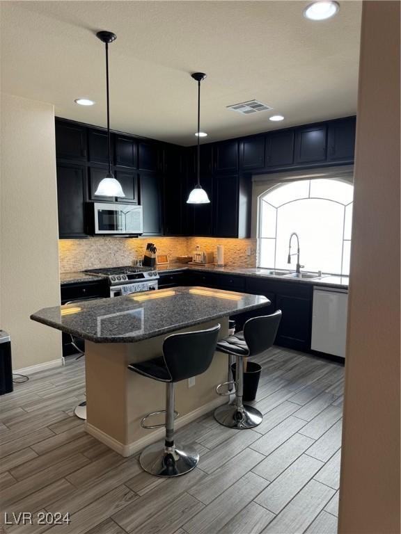 kitchen with stainless steel appliances, visible vents, decorative backsplash, a sink, and a kitchen breakfast bar