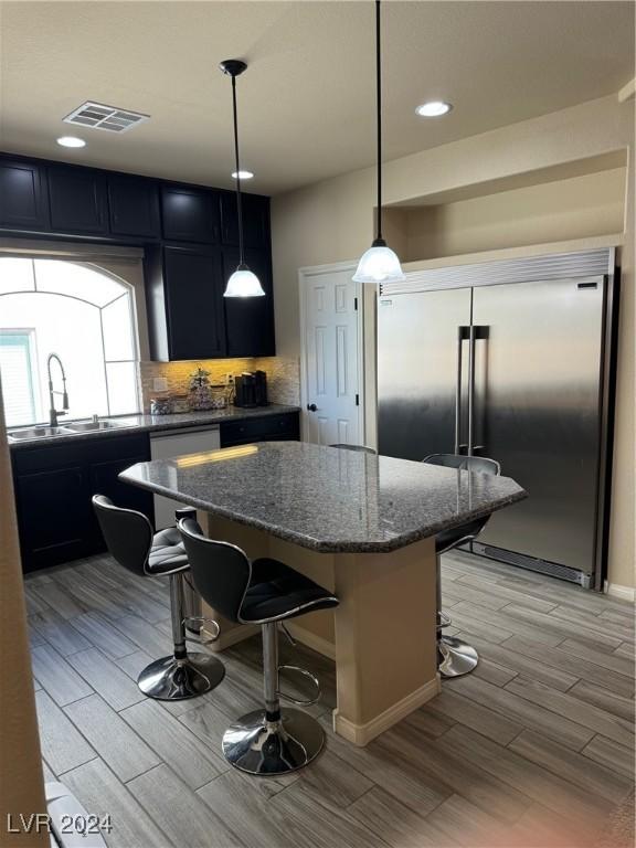 kitchen with visible vents, a breakfast bar area, wood finish floors, a sink, and built in fridge