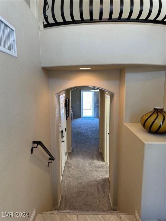 hall featuring visible vents, a high ceiling, arched walkways, and light colored carpet