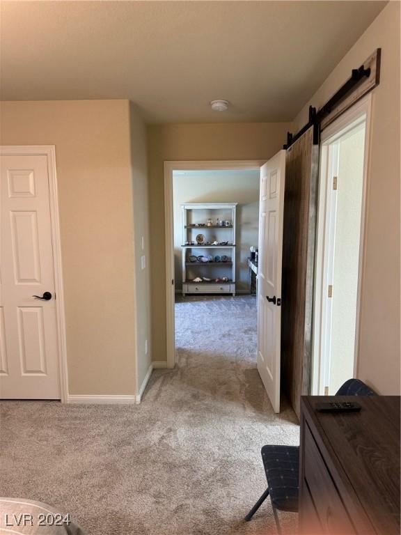 hallway featuring carpet floors, a barn door, and baseboards