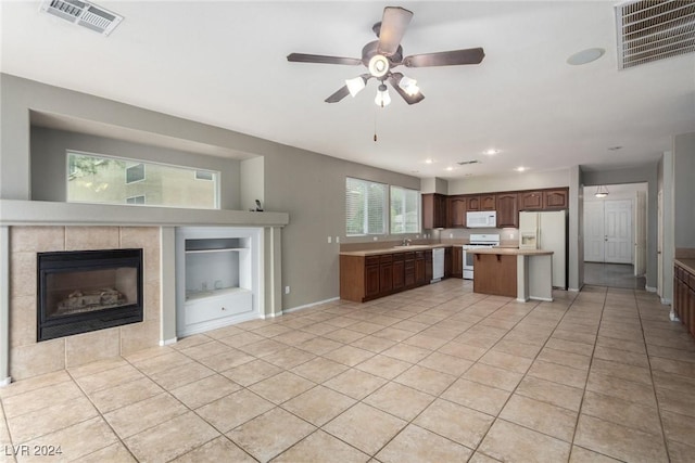 kitchen with sink, white appliances, a breakfast bar area, light tile patterned flooring, and a tiled fireplace