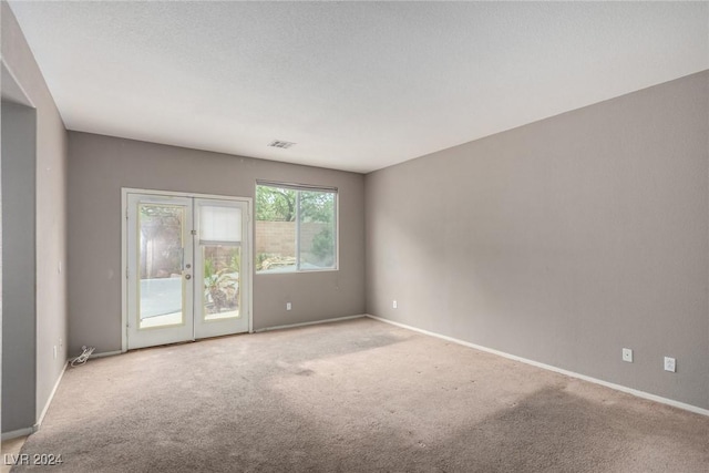 carpeted empty room with a textured ceiling and french doors