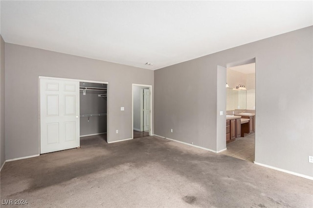 unfurnished bedroom with light colored carpet, ensuite bath, and a closet