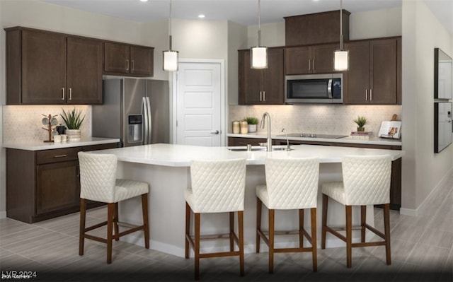 kitchen with pendant lighting, stainless steel appliances, backsplash, and an island with sink