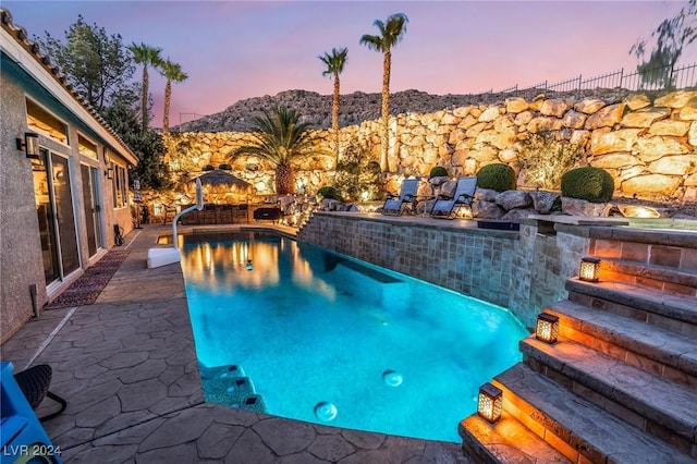 pool at dusk featuring pool water feature and a patio area