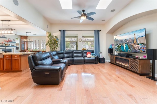 living room with a skylight, ceiling fan, and light wood-type flooring