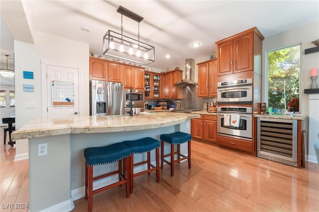 kitchen with wine cooler, stainless steel appliances, a kitchen island with sink, decorative backsplash, and wall chimney range hood