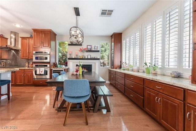 kitchen with an inviting chandelier, light hardwood / wood-style flooring, pendant lighting, decorative backsplash, and wall chimney range hood