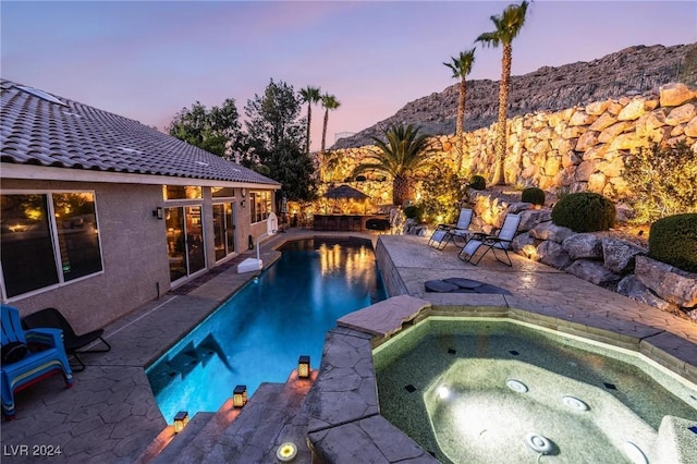 pool at dusk featuring an in ground hot tub, a mountain view, and a patio area