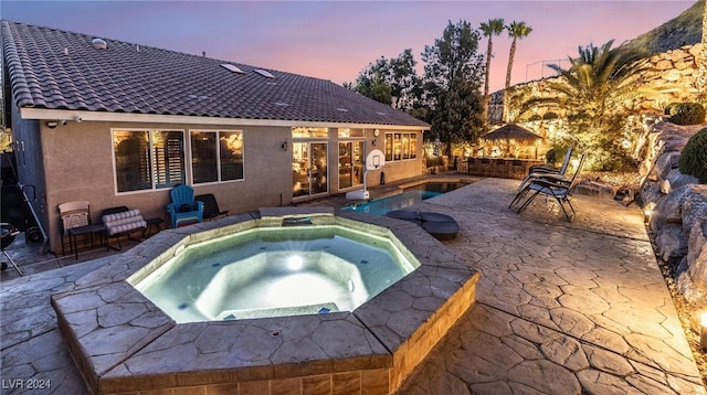 pool at dusk featuring an in ground hot tub and a patio