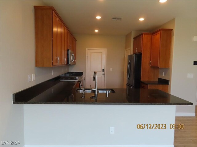 kitchen with sink, kitchen peninsula, black refrigerator, light wood-type flooring, and dark stone countertops