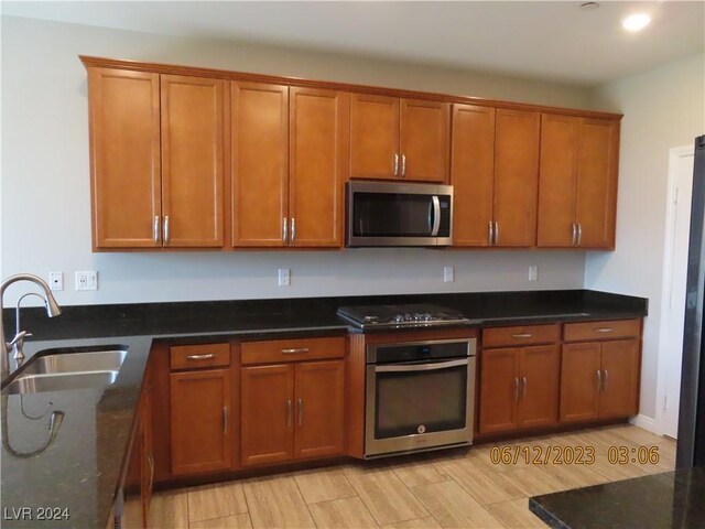 kitchen with sink, dark stone counters, light hardwood / wood-style flooring, and stainless steel appliances