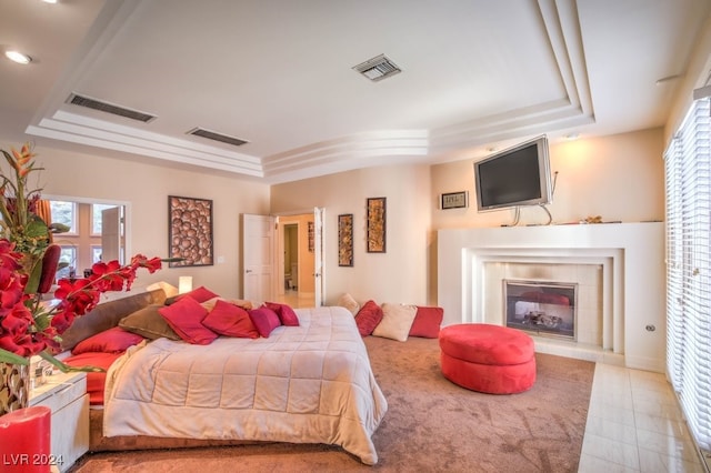 bedroom with a tray ceiling and a tile fireplace