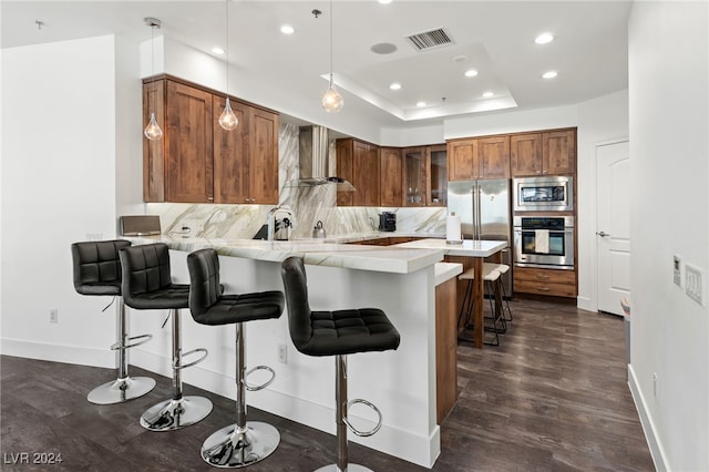 kitchen featuring stainless steel appliances, a peninsula, light countertops, wall chimney exhaust hood, and a kitchen bar