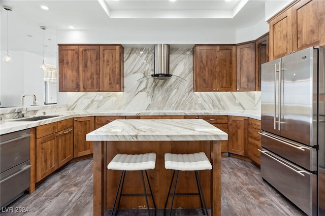 kitchen with high quality fridge, a sink, a kitchen island, brown cabinets, and decorative light fixtures