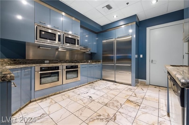 kitchen with built in appliances, blue cabinets, visible vents, marble finish floor, and dark stone countertops