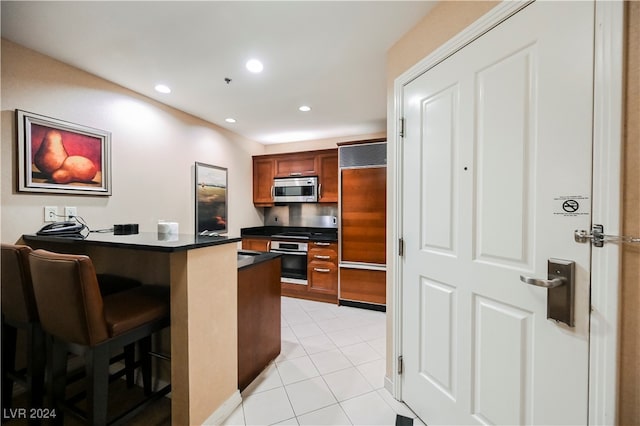 kitchen with stainless steel appliances, kitchen peninsula, light tile patterned floors, and a kitchen bar