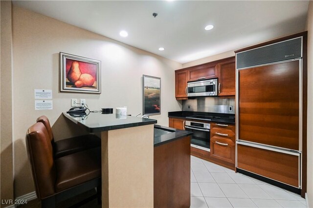 kitchen featuring a kitchen bar, stainless steel appliances, sink, kitchen peninsula, and light tile patterned flooring