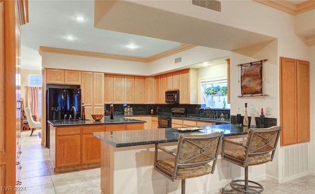 kitchen featuring a kitchen island, dark stone countertops, a kitchen bar, black appliances, and crown molding