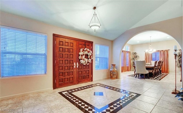 tiled entryway featuring lofted ceiling, plenty of natural light, and a notable chandelier