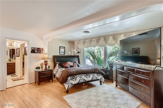 bedroom featuring light hardwood / wood-style flooring, ensuite bath, a textured ceiling, and ornate columns