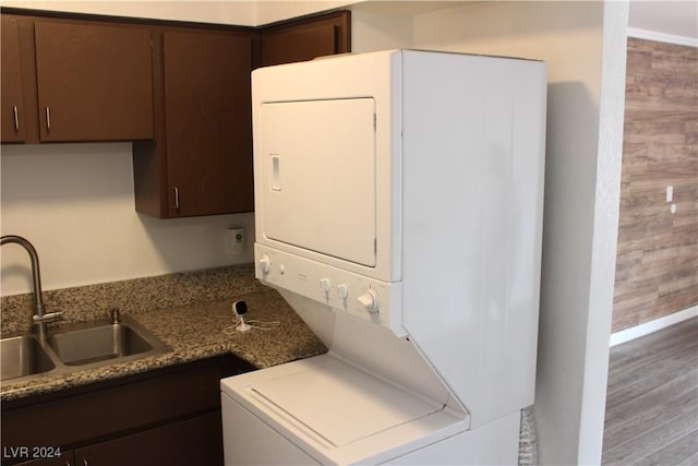 clothes washing area with stacked washer / dryer, wood finished floors, laundry area, and a sink