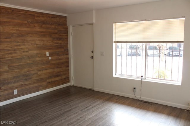 unfurnished room featuring baseboards, wooden walls, and dark wood-style flooring