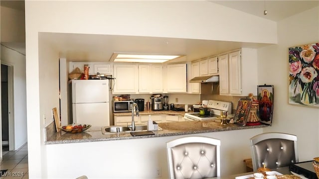 kitchen with a peninsula, white appliances, under cabinet range hood, and a sink