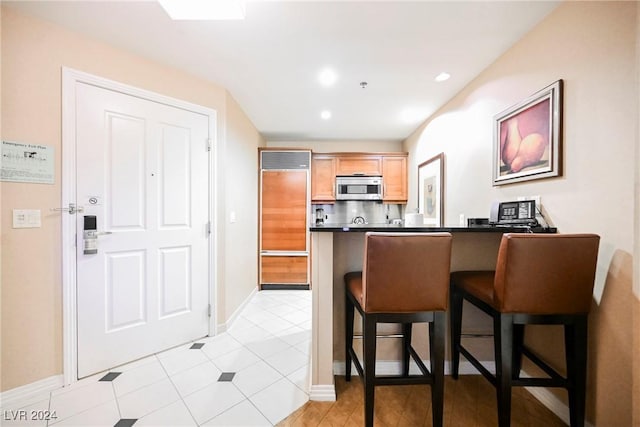 kitchen featuring stainless steel microwave, a breakfast bar area, dark countertops, and a peninsula