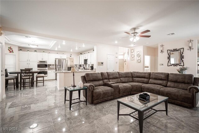 living room with a raised ceiling and ceiling fan