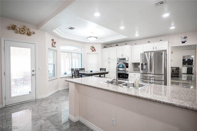 kitchen with appliances with stainless steel finishes, sink, white cabinets, a raised ceiling, and light stone countertops