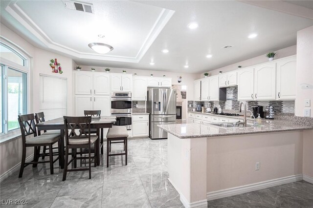 kitchen featuring appliances with stainless steel finishes, sink, white cabinets, light stone counters, and kitchen peninsula