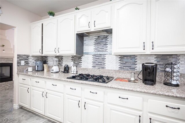 kitchen featuring tasteful backsplash, white cabinetry, light stone countertops, and black gas cooktop