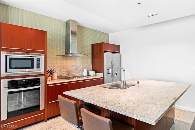 kitchen with sink, wall chimney range hood, stainless steel appliances, an island with sink, and a breakfast bar area