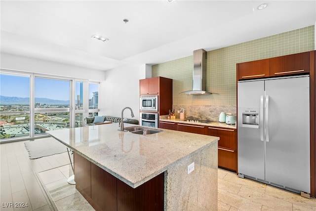 kitchen featuring wall chimney range hood, appliances with stainless steel finishes, a mountain view, and a kitchen island with sink