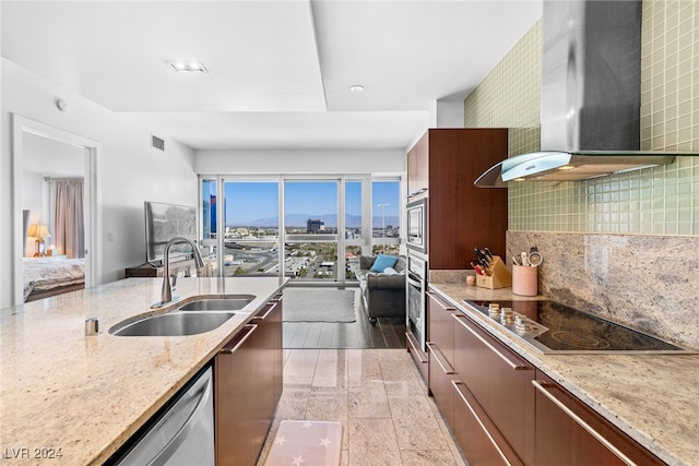 kitchen with sink, backsplash, stainless steel appliances, wall chimney exhaust hood, and light stone countertops