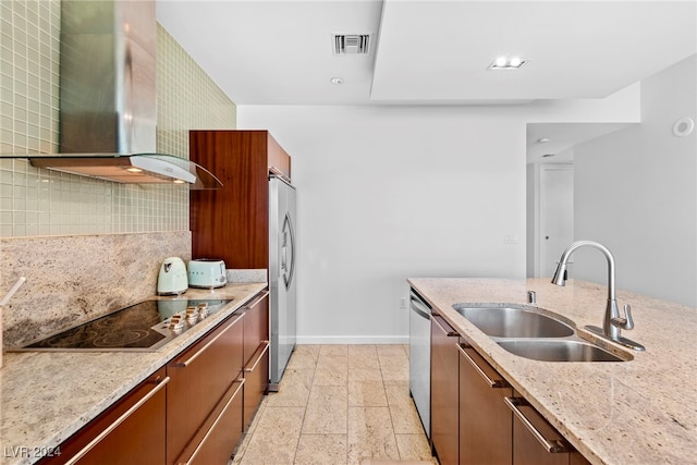 kitchen featuring appliances with stainless steel finishes, tasteful backsplash, wall chimney exhaust hood, light stone counters, and sink