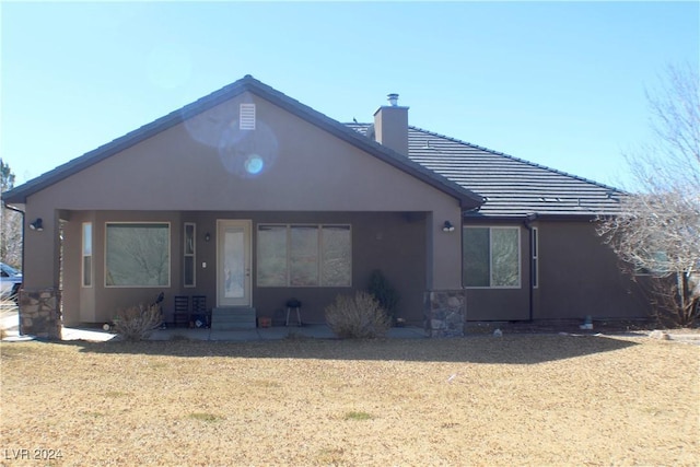 rear view of house featuring entry steps, a tile roof, a chimney, and stucco siding
