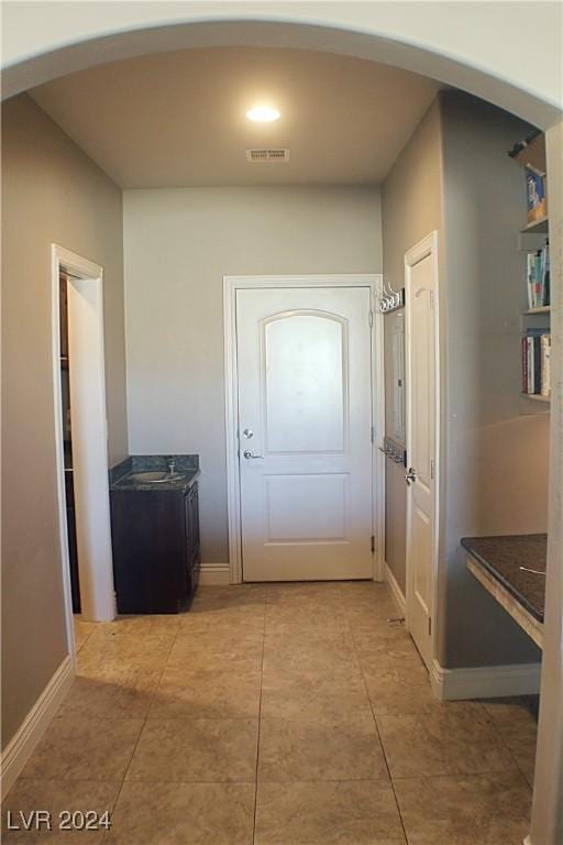 hall featuring arched walkways, light tile patterned flooring, visible vents, and baseboards