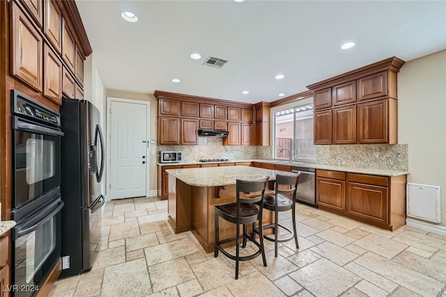 kitchen with light stone countertops, appliances with stainless steel finishes, tasteful backsplash, a breakfast bar, and a center island