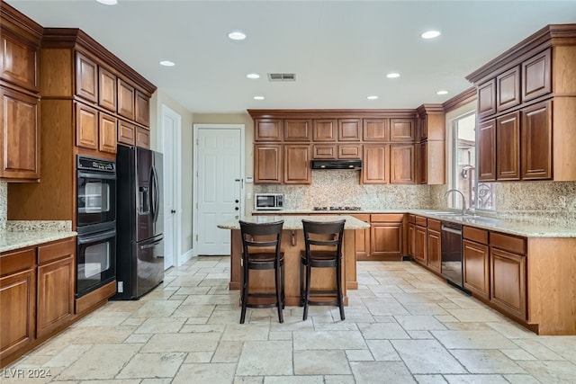 kitchen featuring a kitchen bar, black appliances, decorative backsplash, a kitchen island, and light stone counters