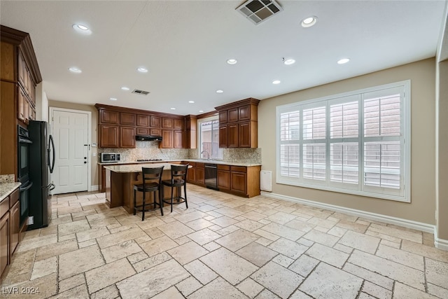 kitchen with a kitchen bar, backsplash, light stone counters, stainless steel appliances, and a center island