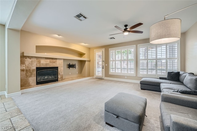 living room featuring carpet floors, built in features, ceiling fan, and a tiled fireplace