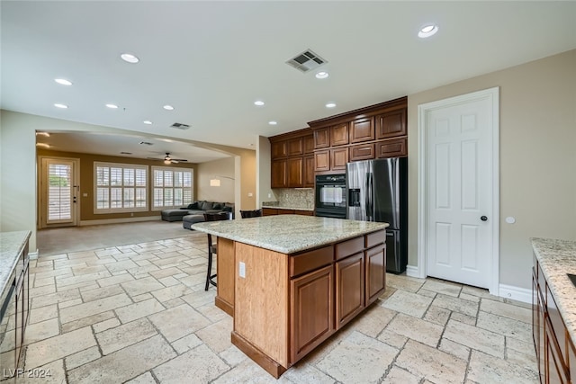 kitchen with stainless steel refrigerator with ice dispenser, light stone counters, ceiling fan, a center island, and oven