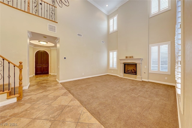 unfurnished living room featuring a healthy amount of sunlight, light tile patterned floors, crown molding, and a high ceiling