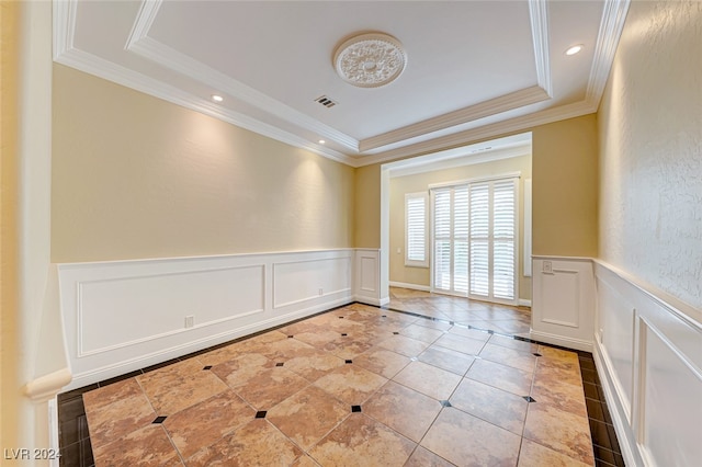 empty room featuring a tray ceiling, ornamental molding, and light tile patterned floors