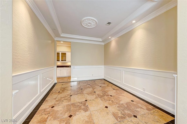 empty room with a decorative wall, wainscoting, visible vents, and crown molding