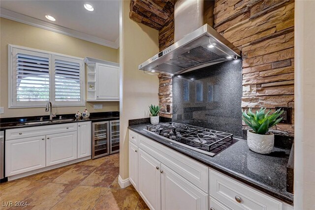 kitchen with stainless steel gas cooktop, wall chimney range hood, sink, white cabinetry, and beverage cooler